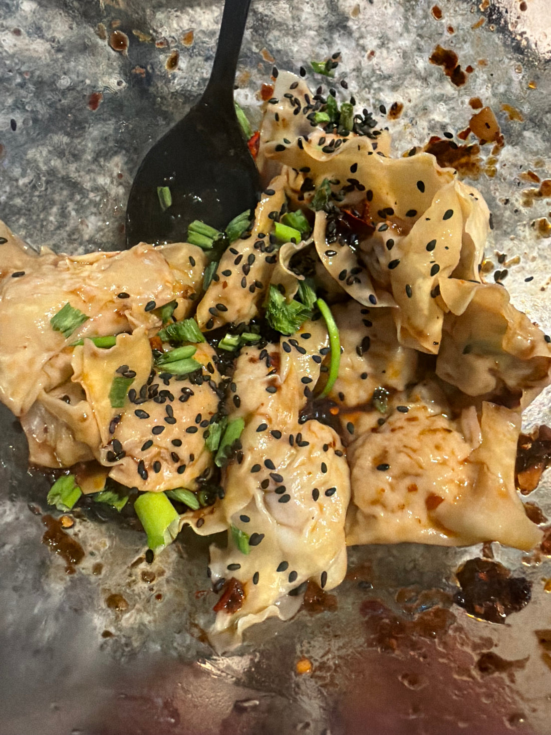 A bowl of Chengdu style pork wontons in red chili oil topped with sliced green onions