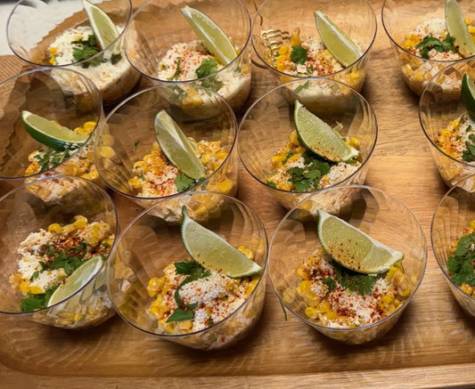 Charred corn kernels in a small cup, topped with crumbled cotija cheese and a dusting of red Tajín seasoning.