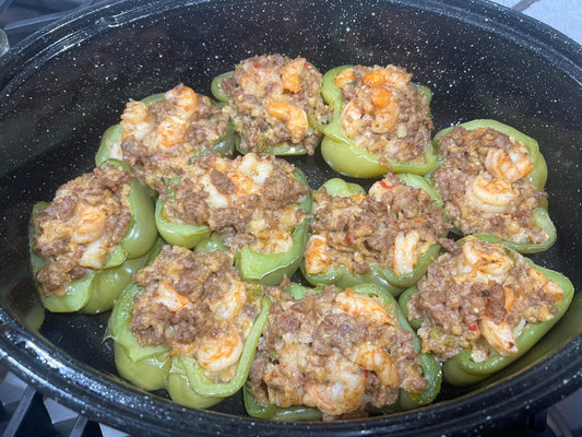 Shrimp and sausage stuffed bell pepper halves in a roasting pan topped with green onions