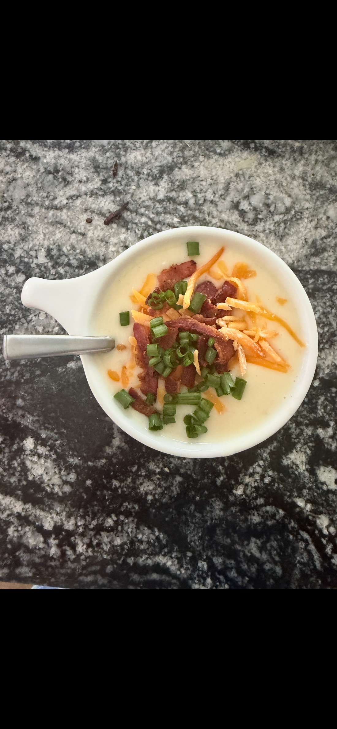 A bowl of baked potato soup topped with bacon, cheddar and green onions