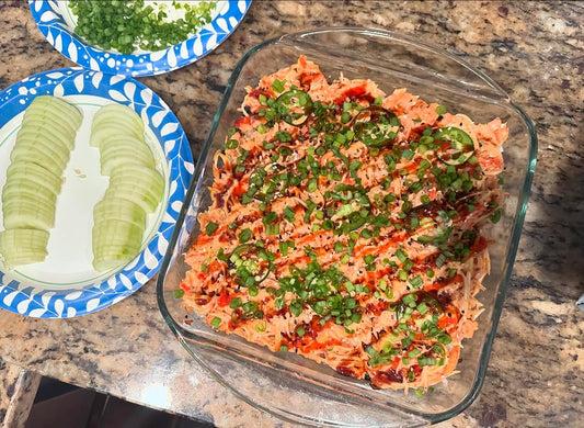 Salmon sushi bake in a baking dish drizzled with Kewpie mayo and sriracha, topped with green onions and sesame seeds