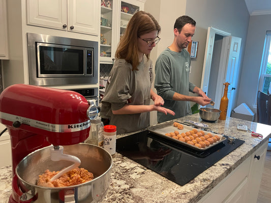 Sausage cheese balls being rolled and placed on a lined baking sheet
