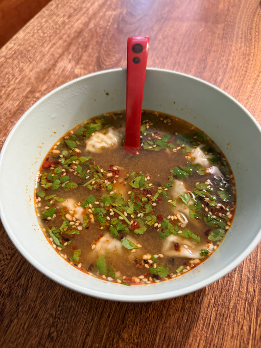 A bowl of dumpling soup with chili oil, furikake and cilantro